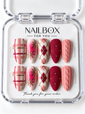Cozy Christmas pink, berry red, and ivory press-on nails with plaid, argyle, gold-tone snowflakes, quilted studs, and raised cable-knit details in a clear nail box.