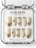 Celeste ivory press-on nails with gold glitter French tips, oval frames, starbursts, pearl-like beads, and raised shell-inspired ridges in a clear nail box.