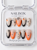 Boo-tiful nude press-on nails with orange and black French tips, white ghosts, spiderwebs, orange pumpkin details, starbursts, and dots in a clear nail box.
