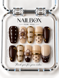 Midnight Affair chocolate brown and nude press-on nails with outlined flowers, gold-tone bands, pearl-like dots, and scalloped French tips in a clear nail box.