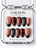 Tortoise Chic blush pink and black press-on nails with amber tortoiseshell patterns, charcoal shimmer, gold-tone oval frames, and starbursts in a clear nail box.