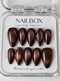 Cocoa Glow chocolate brown press-on nails with copper cat-eye shimmer and sculpted gold borders on two accent nails.