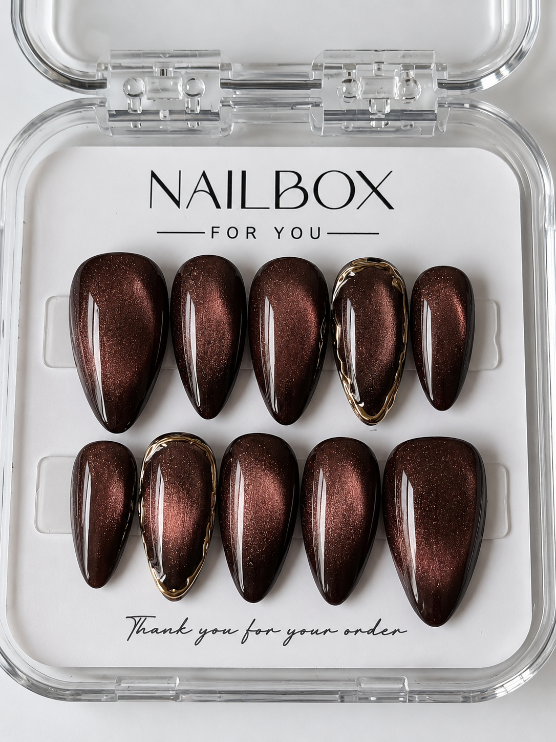 Cocoa Glow chocolate brown press-on nails with copper cat-eye shimmer and sculpted gold borders on two accent nails.