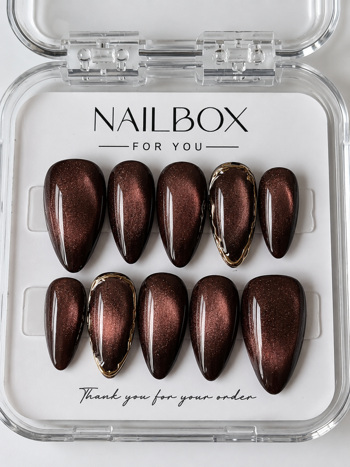 Cocoa Glow chocolate brown press-on nails with copper cat-eye shimmer and sculpted gold borders on two accent nails.