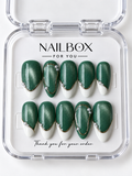 Emerald Glow shimmering green press-on nails with creamy white French tips, gold-tone borders and oval outlines, and pearl-like accents in a clear nail box.
