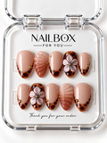 Sandy Kiss peach nude press-on nails with amber tortoiseshell tips, raised blush flowers, shimmering shell-inspired ridges, and gold-tone studs in a clear nail box.