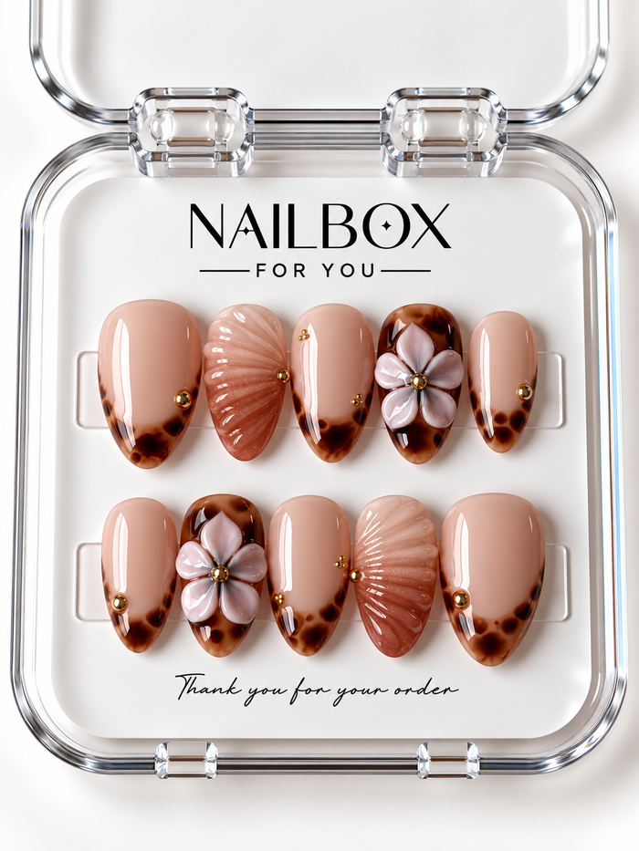 Sandy Kiss peach nude press-on nails with amber tortoiseshell tips, raised blush flowers, shimmering shell-inspired ridges, and gold-tone studs in a clear nail box.