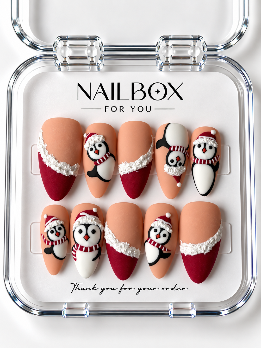 Penguin Party peach nude and red press-on nails with raised penguins wearing Santa hats and striped scarves, plus textured white French-tip trim, in a clear nail box.