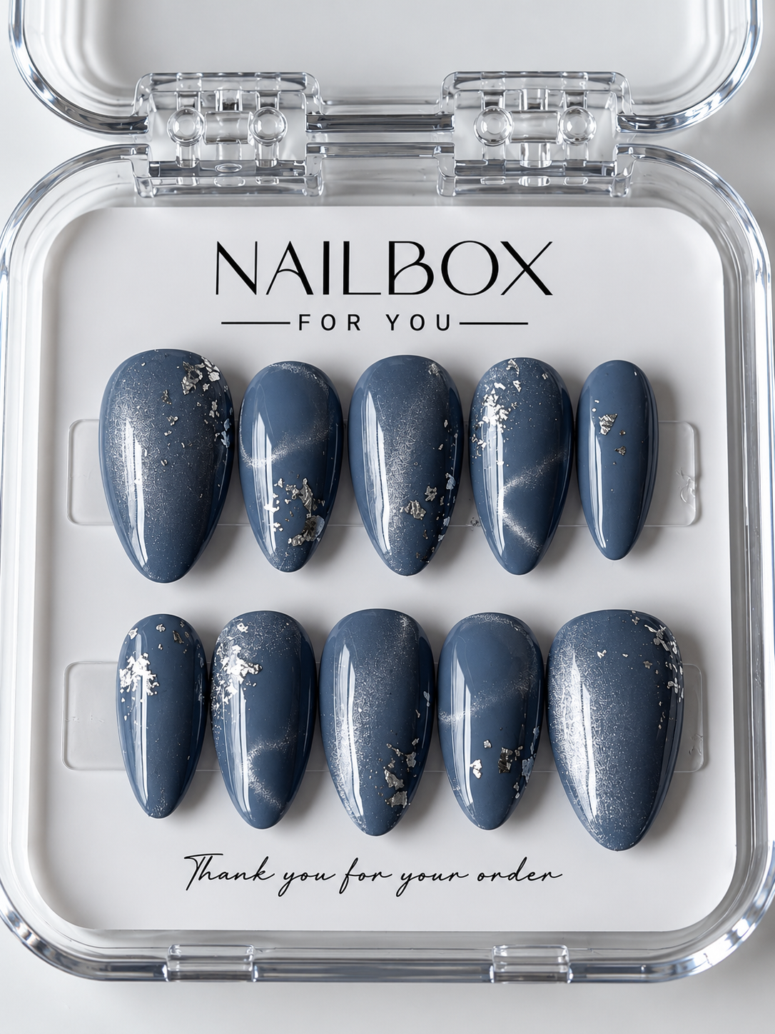 Moonlit smoky blue press-on nails with silver shimmer and scattered silver-tone foil accents, displayed in a clear nail box.