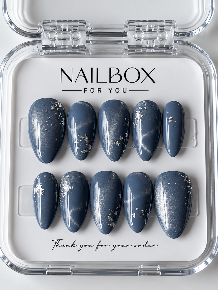 Moonlit smoky blue press-on nails with silver shimmer and scattered silver-tone foil accents, displayed in a clear nail box.