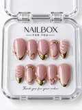 Blushing Pearl blush pink press-on nails with gold-tone tips, oval frames, heart outlines, pearl-like accents, and raised shell-inspired ridges in a clear nail box.