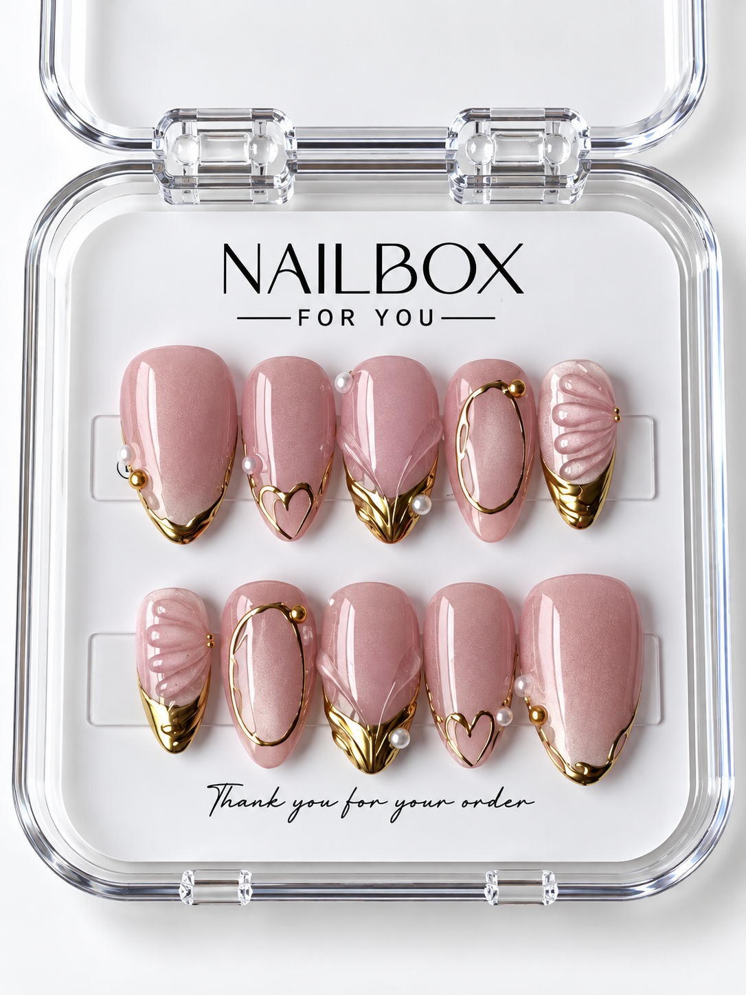 Blushing Pearl blush pink press-on nails with gold-tone tips, oval frames, heart outlines, pearl-like accents, and raised shell-inspired ridges in a clear nail box.