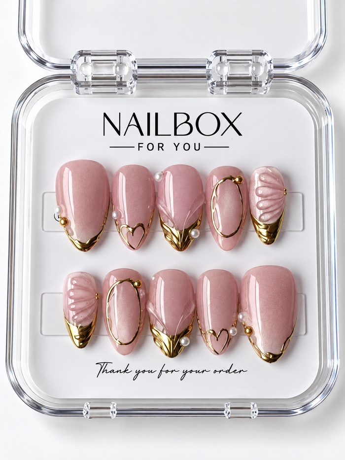 Blushing Pearl blush pink press-on nails with gold-tone tips, oval frames, heart outlines, pearl-like accents, and raised shell-inspired ridges in a clear nail box.