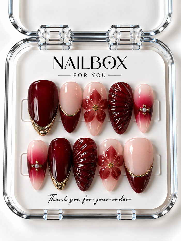 Ruby Romance ruby-red and blush nude press-on nails with raised flowers, fan-like ridges, red gradients, gold-tone borders, and pearl-like accents in a clear nail box.