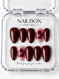 Burgundy Bloom glossy wine-red press-on nails with blush pink accent nails featuring burgundy flowers and tiny gold-tone centers, displayed in a clear nail box.
