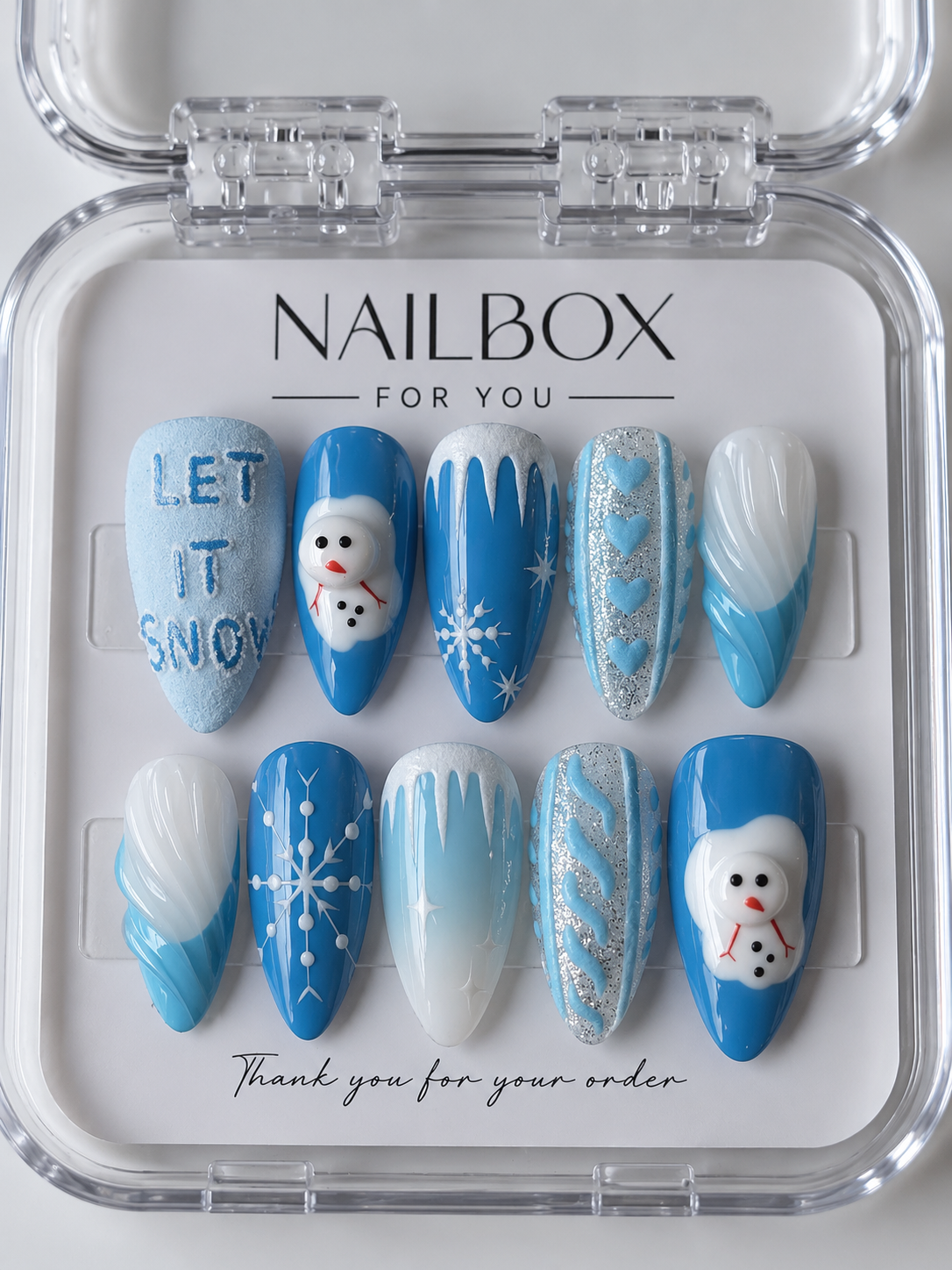 Let It Snow blue and white press-on nails with raised snowmen, snowflakes, icicle drips, silver glitter, and “LET IT SNOW” lettering, displayed in a clear nail box.