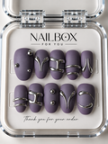 Lilac Rebel matte purple press-on nails with raised silver curves, double bands and round studs, displayed in a clear nail box.