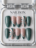 Frosted Evergreen green glitter and nude pink press-on nails with white snowflakes, swirling patterns and silver accents.