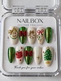 Christmas Charm ivory and green chrome press-on nails with red bows, a pearl-like wreath, Christmas tree, and gift box designs, displayed in a clear nail box.
