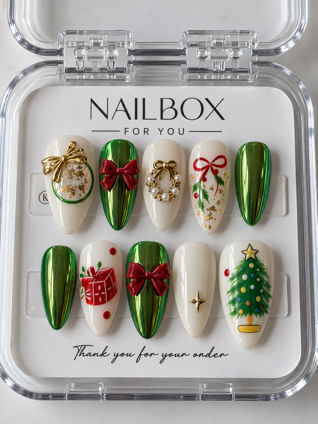 Christmas Charm ivory and green chrome press-on nails with red bows, a pearl-like wreath, Christmas tree, and gift box designs, displayed in a clear nail box.